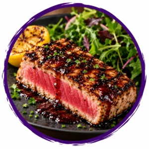 Seared tuna steak with a pink center and pepper crust, served with greens and lemon.